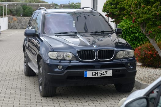 Gaziveren Cyprus -10.04.2025 A sleek dark blue SUV rests on a cobbled road, positioned under a clear sky. Lush greenery frames the scene, creating a serene atmosphere in this tranquil locale.