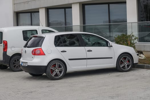 Gaziveren Cyprus -10.04.2025 A sleek white hatchback stands parked at an urban location, alongside a white van. The overcast sky casts a muted light, highlighting the car's sporty wheels against a concrete backdrop.