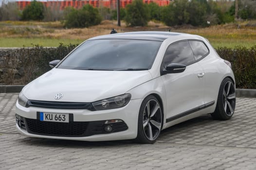 Gaziveren Cyprus -10.04.2025 A sleek white coupe stands proudly on a patterned brick surface, surrounded by lush greenery. The cloudy sky hints at a cool, breezy atmosphere, adding to the scene's tranquility.