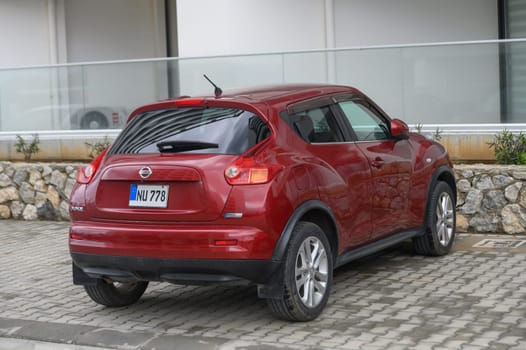 Gaziveren Cyprus -10.04.2025 A sleek red compact SUV rests by a stone wall, reflecting urban style. The vehicle's polished surface glints under the muted light of a cloudy afternoon, inviting admiration.