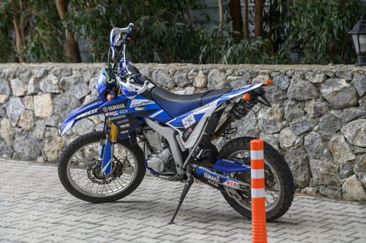 Gaziveren Cyprus -10.04.2025 A powerful off-road motorcycle rests against a sturdy stone wall, showcasing its sleek design. The tranquil setting features lush greenery, hinting at nearby adventure.