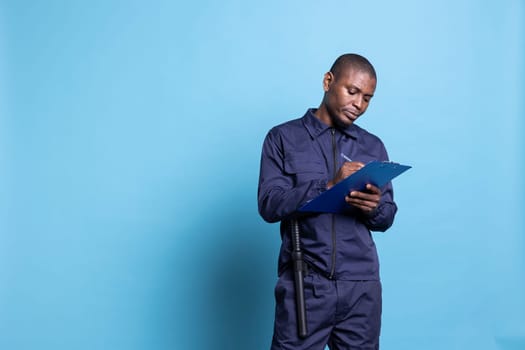 Mall security officer takes notes on his clipboard files while on duty, ensuring safety and protection on the premises. Trained guard writing list of attendees for an event, defense responsibility.