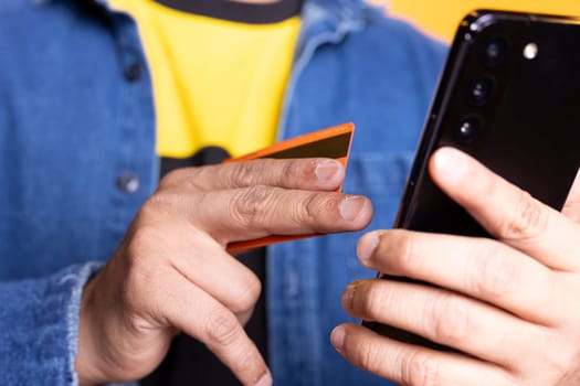 Young person with man bun adding payment method on shopping website, entering credential and confirming money transfer after shopping online against orange background. Upbeat guy.