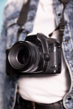 Extreme closeup of a black camera. Selective focus on DSLR hanging from the neck of an individual in a denim jacket, with selective focus on the lens, highlighting intricate details.