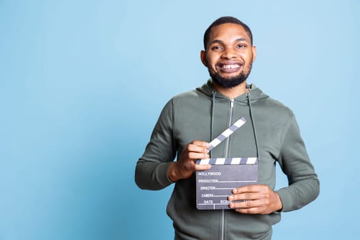 African american positive guy presenting his filming slate for movie industry, cinematography and entertainment with the producer or director clapperboard. Happy confident filmmaker.