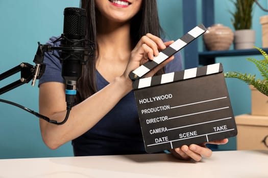 Closeup of woman in vlogging studio presenting a clapperboard to the camera, using a microphone for her product review. The scene captures the essence of digital content creation and media production.