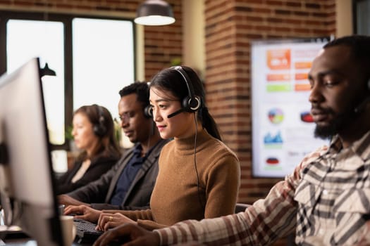 Multiethnic call center agents sit at their workstations, handling business inquiries and communicating with remote customers. Coffee, computers, and headsets set the office scene.