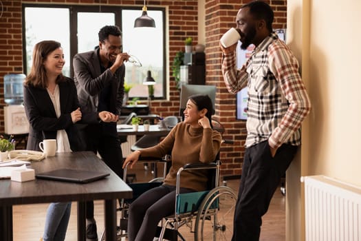 Colleagues enjoying casual office chatter, bonding over shared experiences in modern startup environment. Laughter fills the modern workspace as multiethnic employees take a break at the office desk.