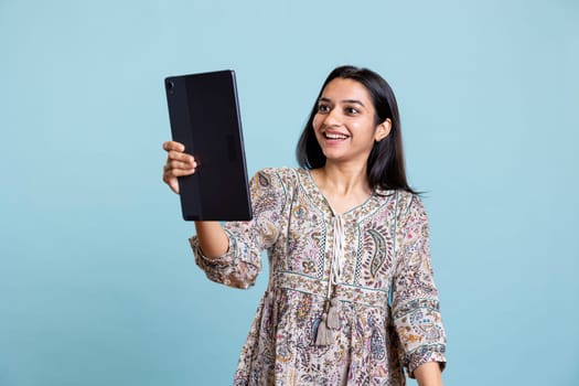 Jolly indian person chatting with her friend over video conference online, enjoying relaxation time in studio. Upbeat girl communicating with mate using phone, video call connection.