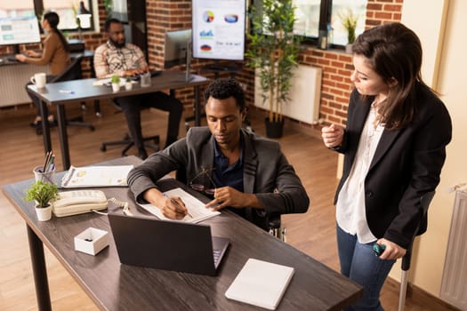 Businesswoman with a crutch collaborating with a colleague in wheelchair, sharing insights on marketing strategies. Diverse entrepreneurs with disabilities having a discussion in brick wall workspace.
