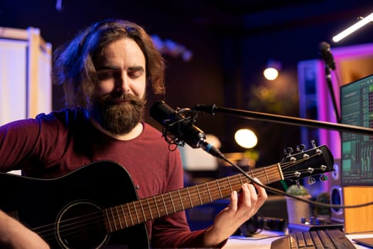 Skilled composer playing acoustic guitar and singing on microphone in home studio, mixing and mastering songs with electronic tools. Music producer recording tunes on daw software.