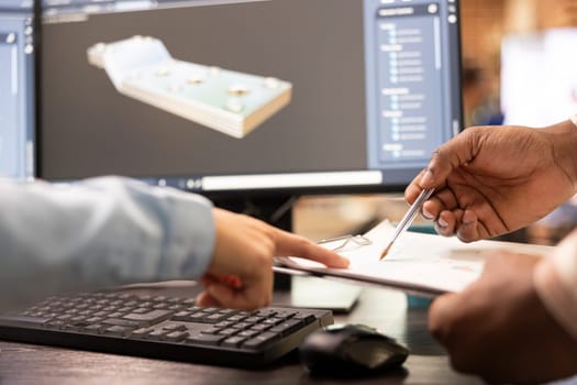 Closeup of multiethnic developers reviewing a sketch plan with 3D software displayed on computer monitor. Selective focus on diverse hands touching a clipboard, analyzing tool sizing numbers.