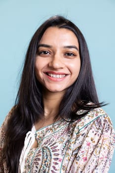 Portrait of smiling indian person posing in front of the camera, being happy and confident in herself. Upbeat friendly woman with long hair standing against blue background, freshness.