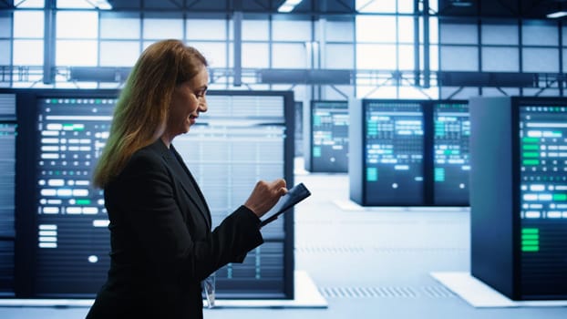 Technician doing checkup using tablet to prolong data center electronics life span and avoid downtime. Employee walking in server room, monitoring server infrastructure using digital device, camera B