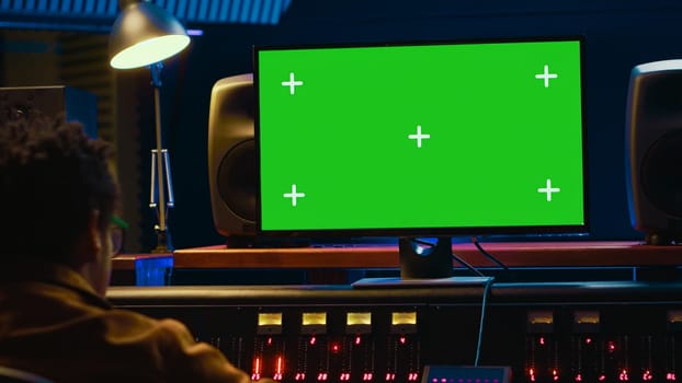 African american sound designer looks at greenscreen to record and edit tunes, uses mixing console to create new songs. Skilled technician works on processing and track recording. Camera A.