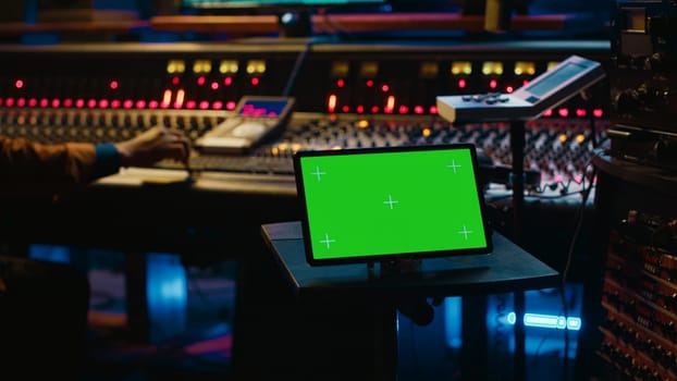 African american tracking engineer works with greenscreen, operates audio console with moving faders and colored meters. Specialist pressing buttons and faders to edit audio recordings. Camera A.
