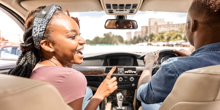 Back view of happy black lovers sitting in nice car, going vacation together by car. Cheerful african american millennial man and woman enjoying trip, having conversation, laughing