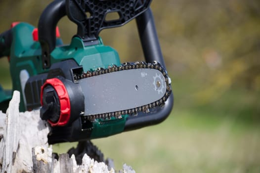 A close-up image features a modern, battery-powered chainsaw, highlighting its chain, bar, and ergonomic design elements against a blurred background.