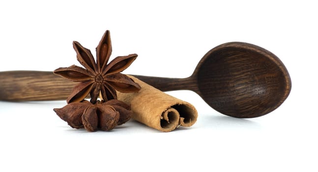 Aromatic star anise and a cinnamon stick rest next to a rustic wooden spoon on a clean, white surface, capturing a sense of culinary warmth.