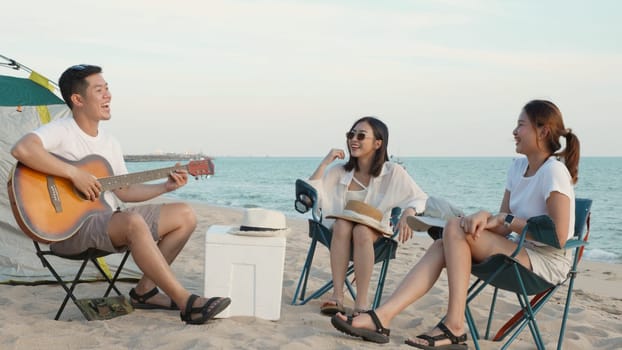 Happy friend have fun playing guitar and clap in camp they smiling together in holiday on sand beach near camping tent vacation time at sunset, Young Asian group woman and man in summer travel outdoor