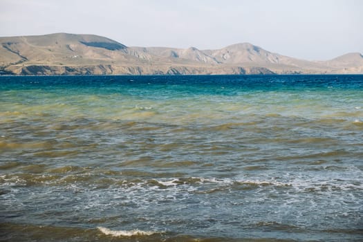 Polluted sea washing Crimean coast with brown waves and mountains in the background