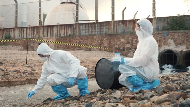 Ecologist sampling water from the river with test tube, Scientist or Biologist in a protective suit and protect mask collects sample of waste water from industrial for analyze, problem environment