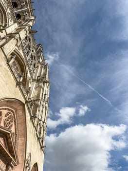 A Gothic cathedral facade towers into a blue sky with clouds, showcasing historical grandeur and intricate architecture.