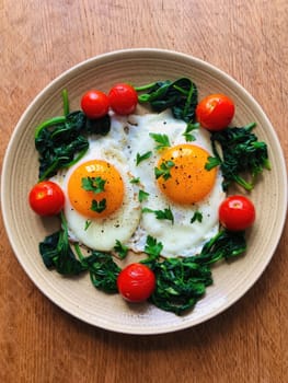 Two sunny side up eggs are placed on a bed of sautéed spinach with cherry tomatoes surrounding them. Fresh parsley adds a touch of color to this nutritious breakfast dish.