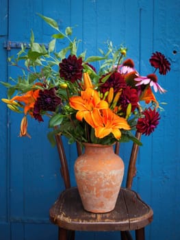 A vibrant bouquet filled with orange lilies, dark red dahlias, and purple echinacea is elegantly displayed in a clay vase.
