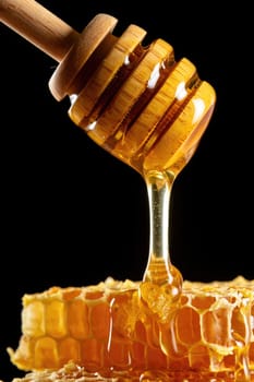 Sweet golden honey flows gracefully from a wooden stick, touching a hexagonal honeycomb below. The dark background enhances the rich color and texture of the honey, creating an inviting appearance.