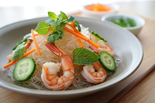 A vibrant plate of shrimp salad showcases fresh cooked shrimp, glass noodles, and colorful vegetables like cucumber and carrots. Garnished with mint leaves, it looks healthy and appetizing.