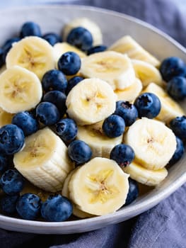 Slices of ripe banana are combined with plump blueberries in a bowl, creating a vibrant and healthy fruit salad. Ideal for a refreshing snack or breakfast option.