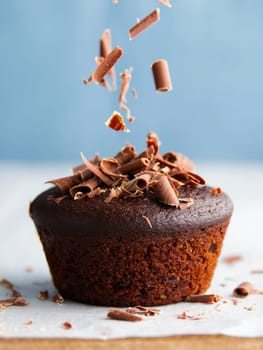 A freshly baked chocolate muffin is showcased with chocolate curls sprinkling down from above.