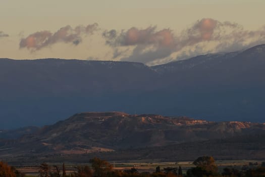 As dusk approaches, soft pastel clouds drift above the rugged peaks, creating a serene atmosphere over the expansive landscape filled with rolling hills and distant mountain ranges.