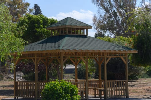 Amidst lush greenery, a beautifully crafted wooden gazebo stands invitingly. Sunlight filters through the trees, creating a tranquil retreat perfect for relaxation and gatherings.