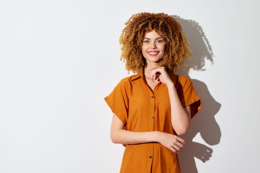 Smiling young woman with voluminous curly hair, dressed in a brown shirt, poses against a plain white backdrop Her cheerful demeanor and stylish look evoke feelings of happiness and positive energy