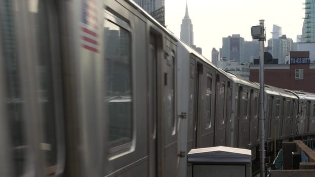 New York City, United States - 2 Sept 2023: Subway station. Metro train public transportation platform. Elevated outdoor railway, Queens passenger railroad traffic, Long Island. Empire State building.