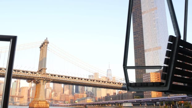 New York City, United States - 7 Sept 2023: Manhattan Bridge to Brooklyn. Pier 35 swings bench, waterfront downtown skyline cityscape. World Trade Center skyscraper, financial district morning sunset.