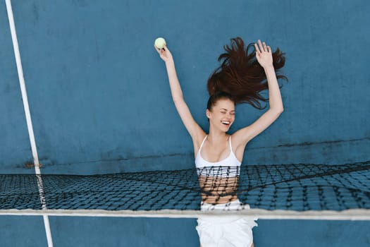 Happy female athlete expressing victory on a tennis court, wearing a stylish white ensemble, with a vibrant blue background, ideal for sports and fitness promotions