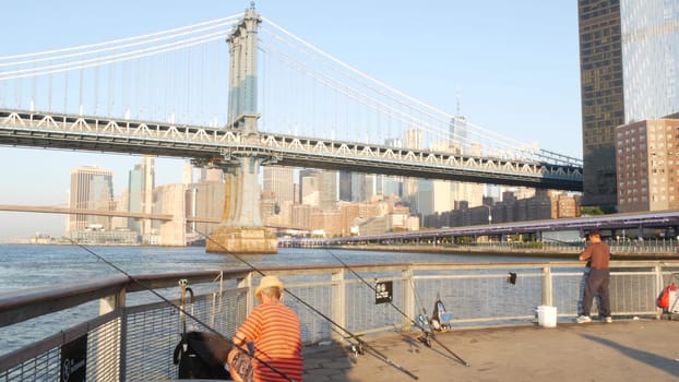 New York City, United States - 7 Sept 2023: Manhattan Bridge. Fisherman near Pier 35 swings, waterfront downtown skyline cityscape. World Trade Center skyscraper, people fishing and morning sunset.