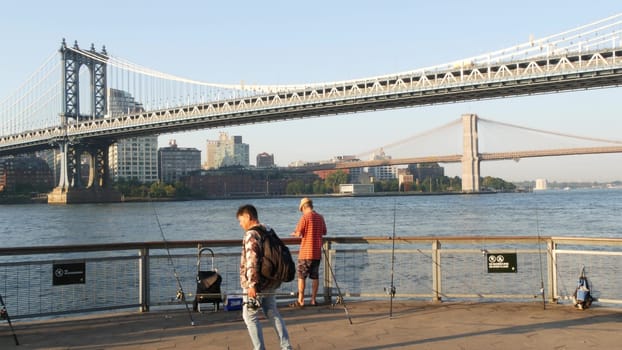 New York City, United States - 7 Sept 2023: Manhattan Bridge, Brooklyn Dumbo. East river waterfront skyline cityscape, fishermen on riverfront Pier 35. People and morning sunset, men fishing by water.
