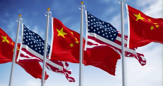 3D render of Chinese and American flags waving side by side in the wind, symbolizing diplomacy, patriotism and international relations under a clear sky.