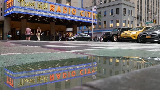 New York, United States - 10 Sept 2023: Manhattan Midtown street. Radio City Music Hall, Rockefeller Center, USA. People pedestrian, urban traffic, 6 Sixth Americas avenue crossroad, yellow taxi cab.