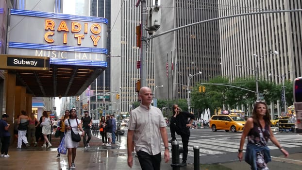 New York, United States - 10 Sept 2023: Manhattan Midtown street. Radio City Music Hall, Rockefeller Center, USA. People pedestrian, urban traffic, 6 Sixth Americas avenue crossroad, yellow taxi cab.