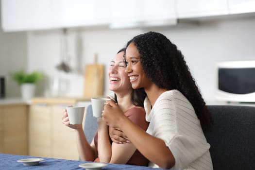 Happy interracial couple laughing drinking coffee in the kitchen at home