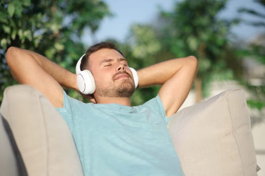 Happy man wearing headphone listening music sitting in a terrace a sunny day
