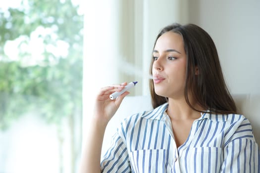 Woman vaping and blowing smoke sitting on a couch at home