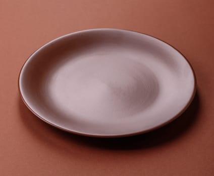 Empty ceramic plate on a monochrome brown background. Empty plate with cutlery on a dining table