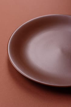 Empty ceramic plate on a monochrome brown background. Empty plate with cutlery on a dining table