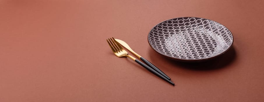 Empty ceramic plate on a monochrome brown background. Empty plate with cutlery on a dining table